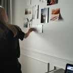 Woman arranging photos on wall in modern office, laptop on desk, creative workflow.